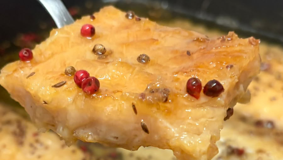 Fotografia registra uma fatia de uma fatia de uma comida amarela com sementes vermelhas sobre a fatia.