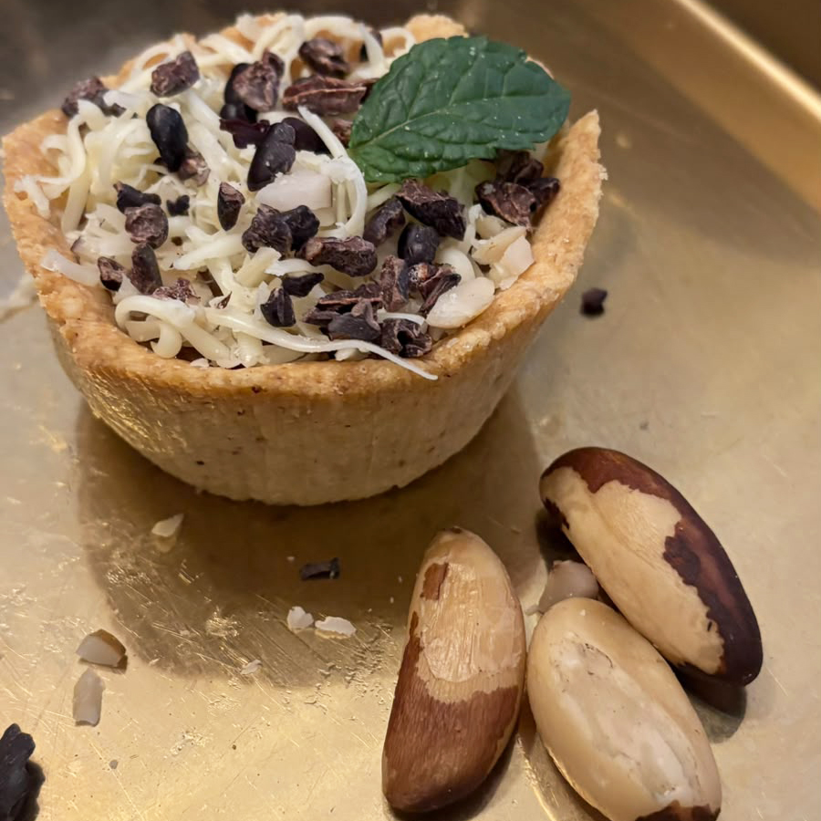 Fotografia registra uma tartelete com recheio de chocolate e tiras de castanha do pará. Ao lado do doce, há três castanhas do Pará.