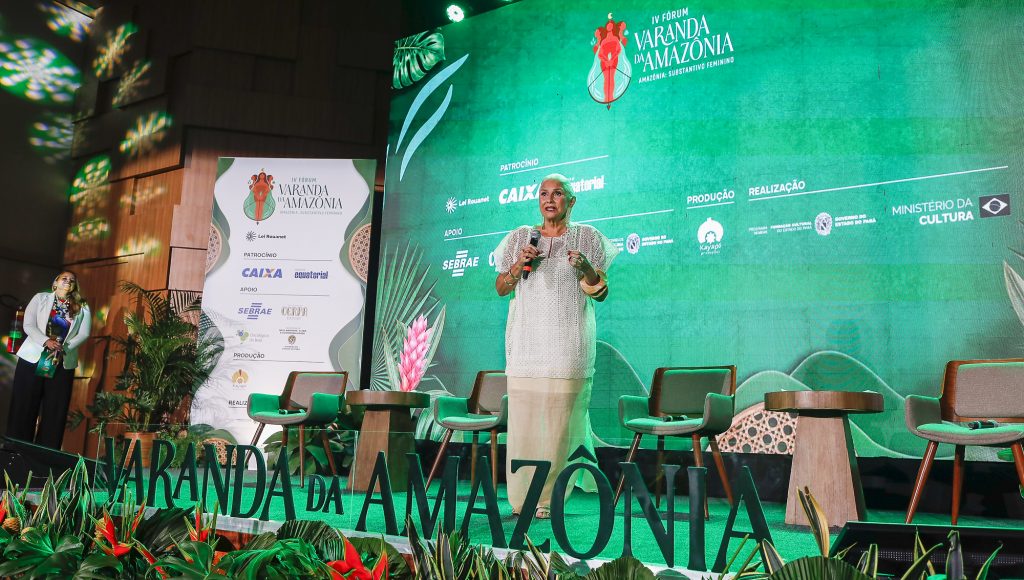 Fotografia registra a cantora Fafá de Belém, falando ao microfone, do palco de uma evento.